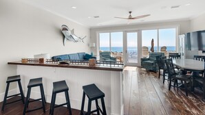 A spacious kitchen with a bar area, large windows, and a view of the ocean. - White Sands 451- Beach Dreams (Pensacola Beach)