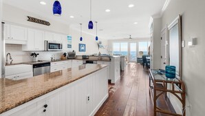 A modern kitchen with white cabinets, granite countertops, and blue pendant lights. - White Sands 451- Beach Dreams (Pensacola Beach)