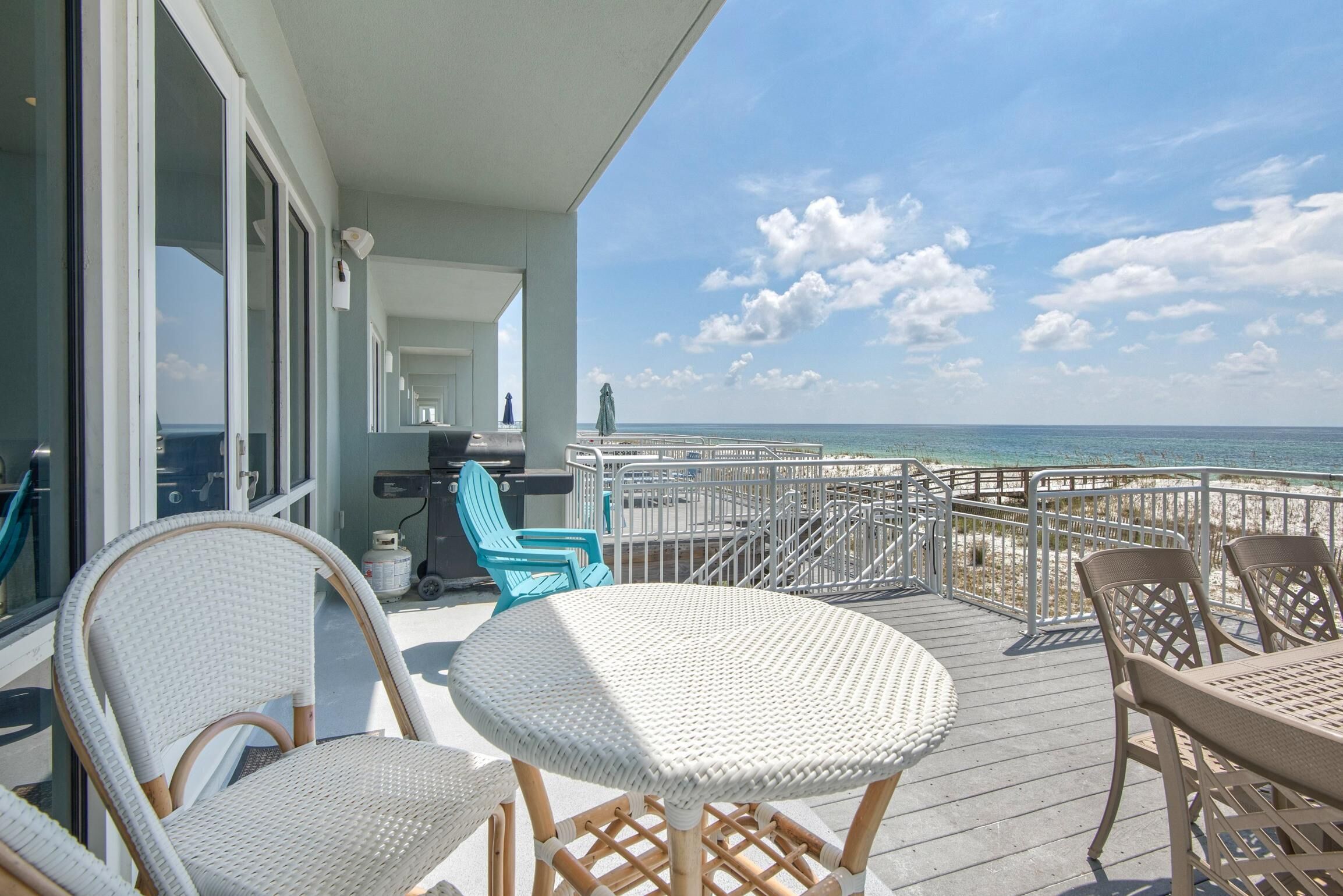 A deck with wicker furniture, a grill, and a view of the ocean.