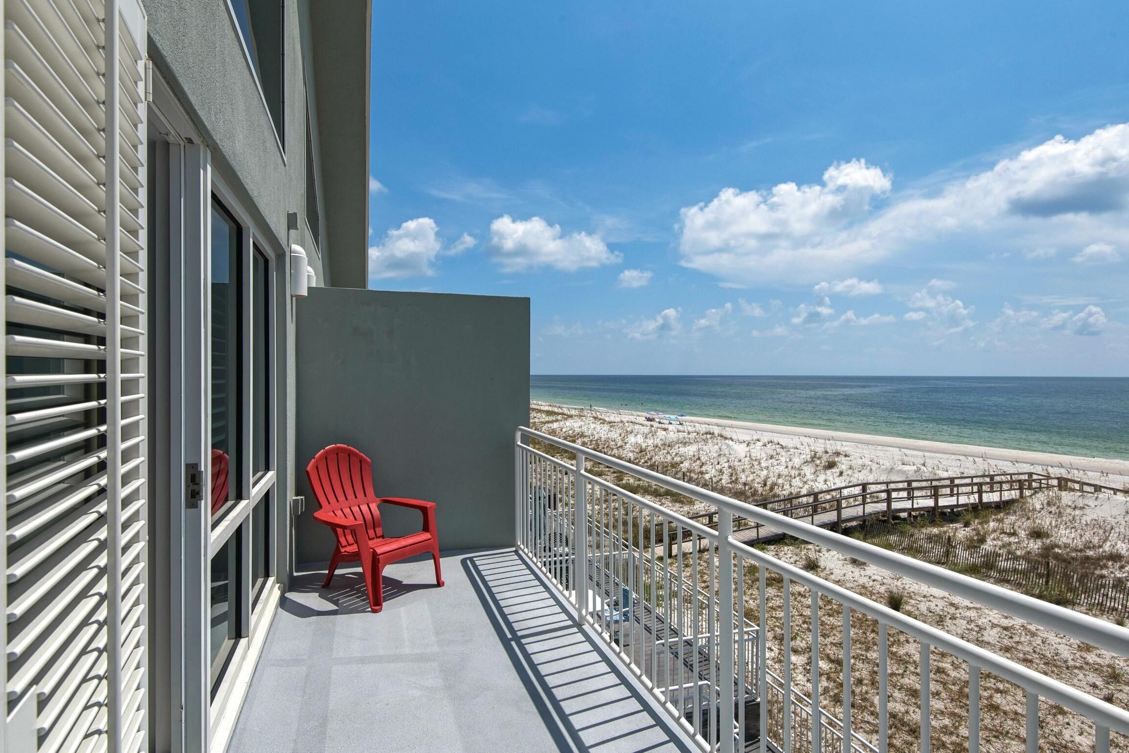 A balcony with a red chair, a view of the beach, and a clear sky.