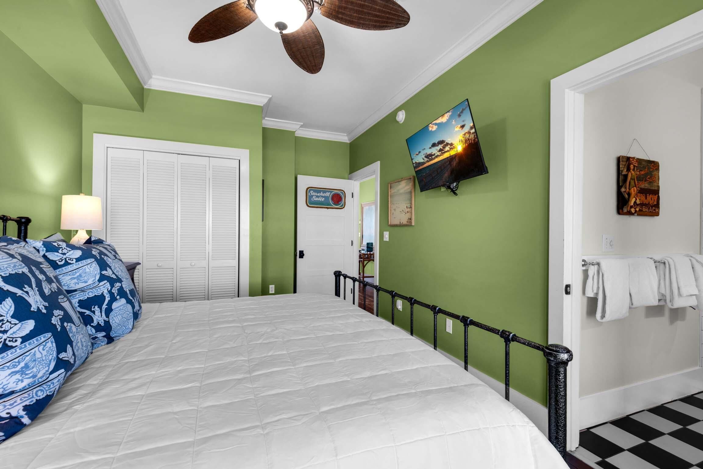 A bedroom with a bed, a ceiling fan, a television, and a door with a towel rack.