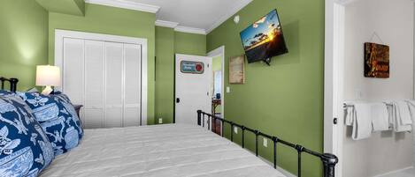 A bedroom with a bed, a ceiling fan, a television, and a door with a towel rack.