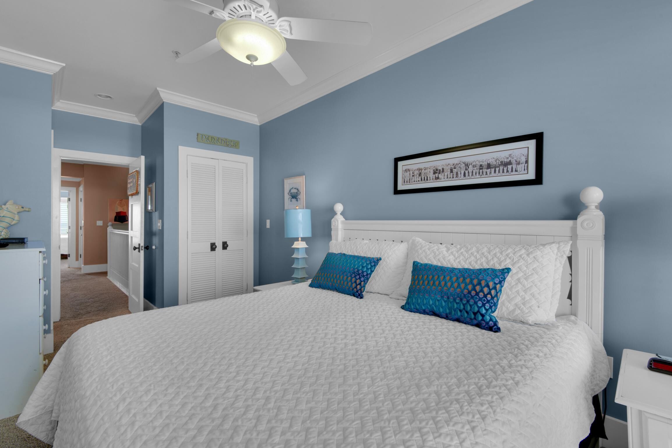 Ein Schlafzimmer mit einem weißen Bett, blauen Wänden und einem Deckenventilator.