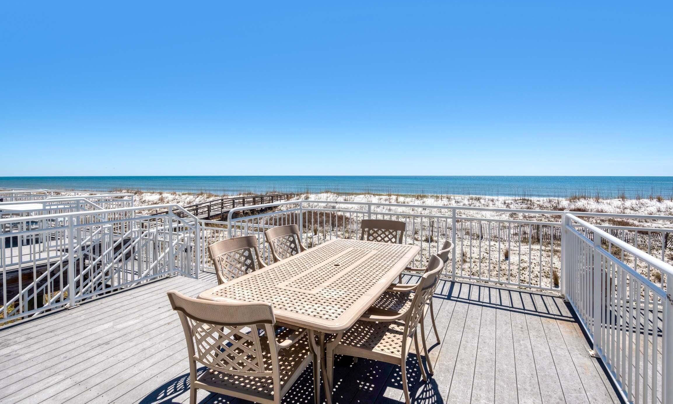 A wooden deck with a table and chairs overlooking a beach.