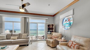 A spacious living room with a large window overlooking the ocean, a ceiling fan, and a view of the beach. - Seahorse Unit R (Pensacola Beach)