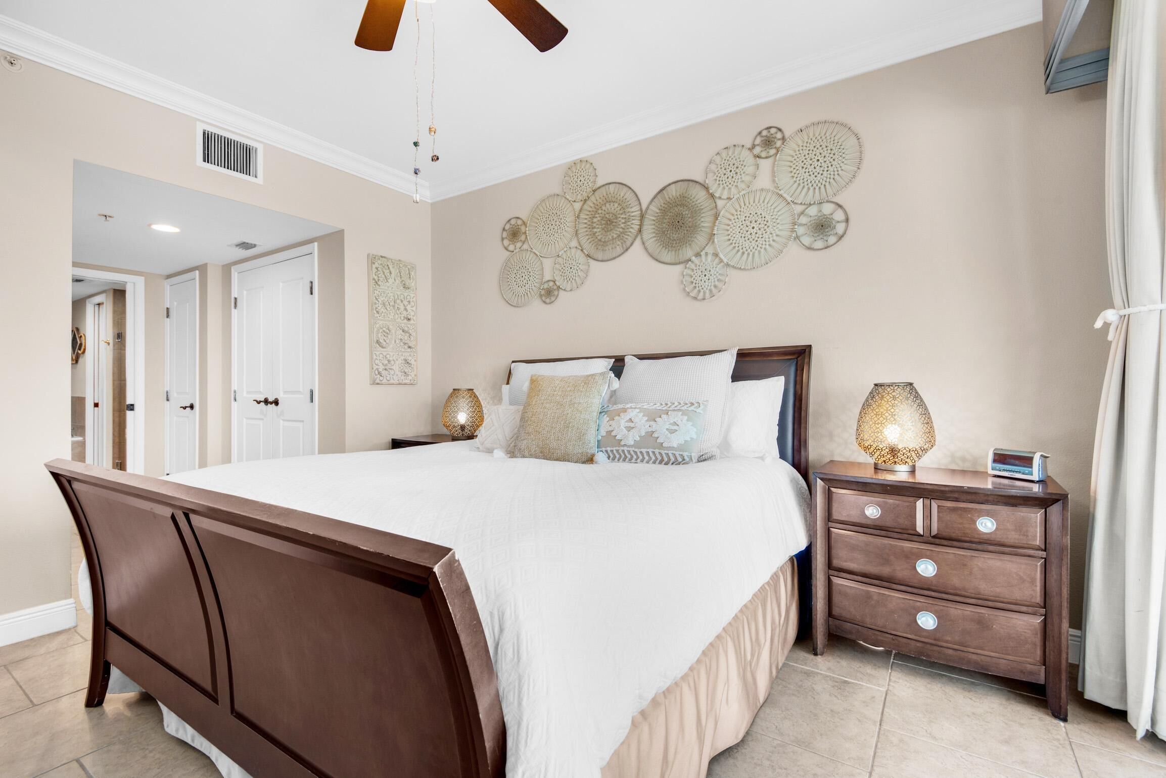 A bedroom with a large bed, a nightstand with a lamp, and decorative wall art.