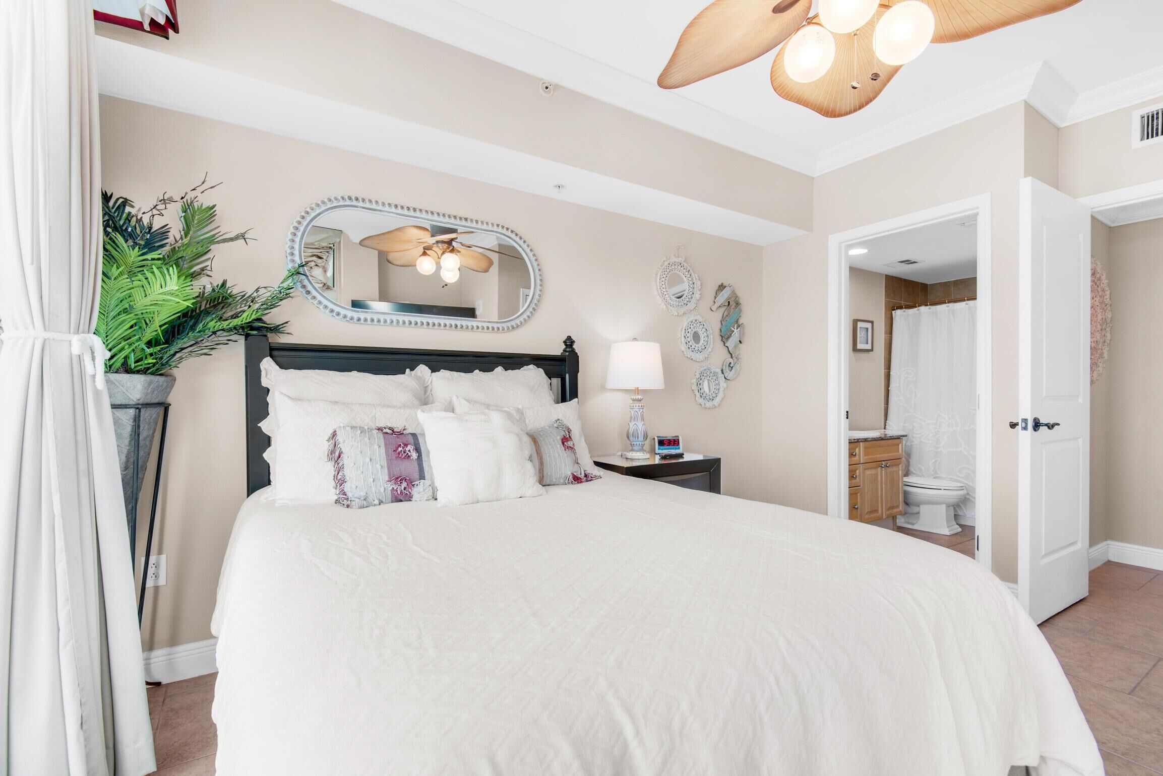 Quarto com cama grande, mesa de cabeceira, espelho e ventilador de teto.