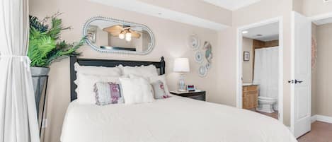 Quarto com cama grande, mesa de cabeceira, espelho e ventilador de teto.