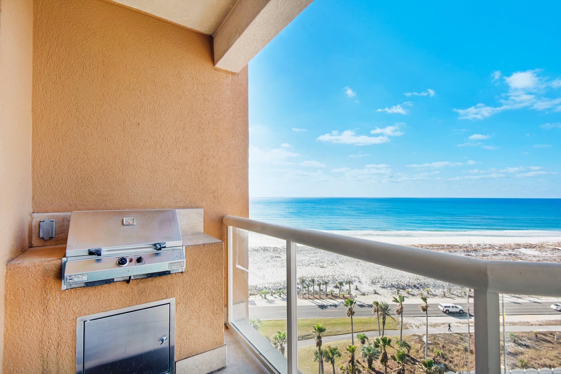 A balcony with a grill and a view of the beach.