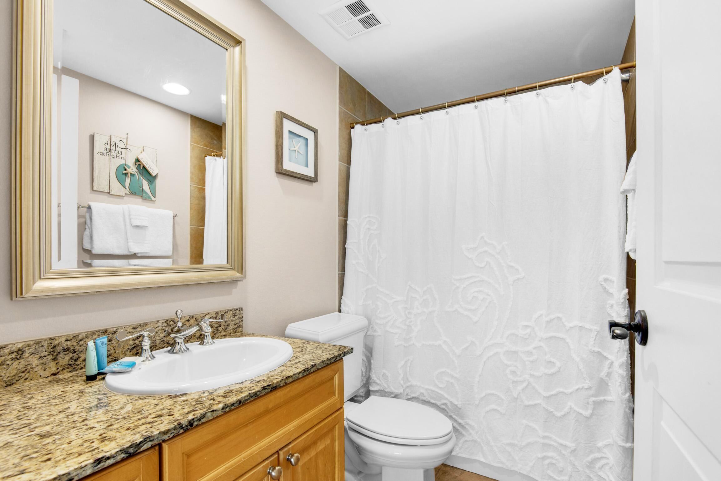 A bathroom with a granite countertop sink, a white toilet, and a shower curtain.