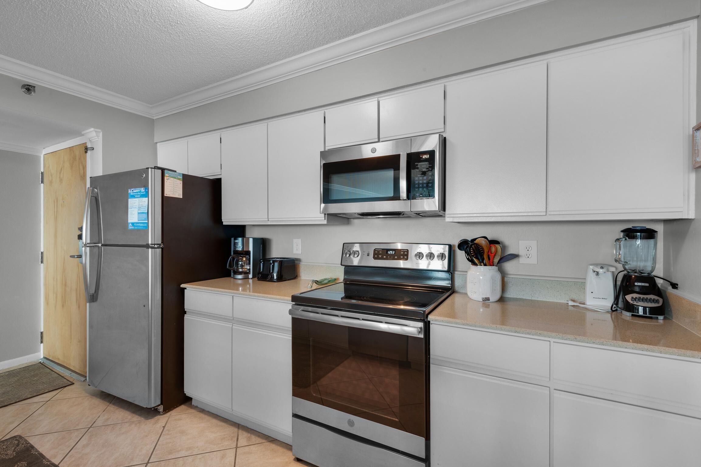 A modern kitchen with stainless steel appliances, white cabinetry, and a wooden door.
