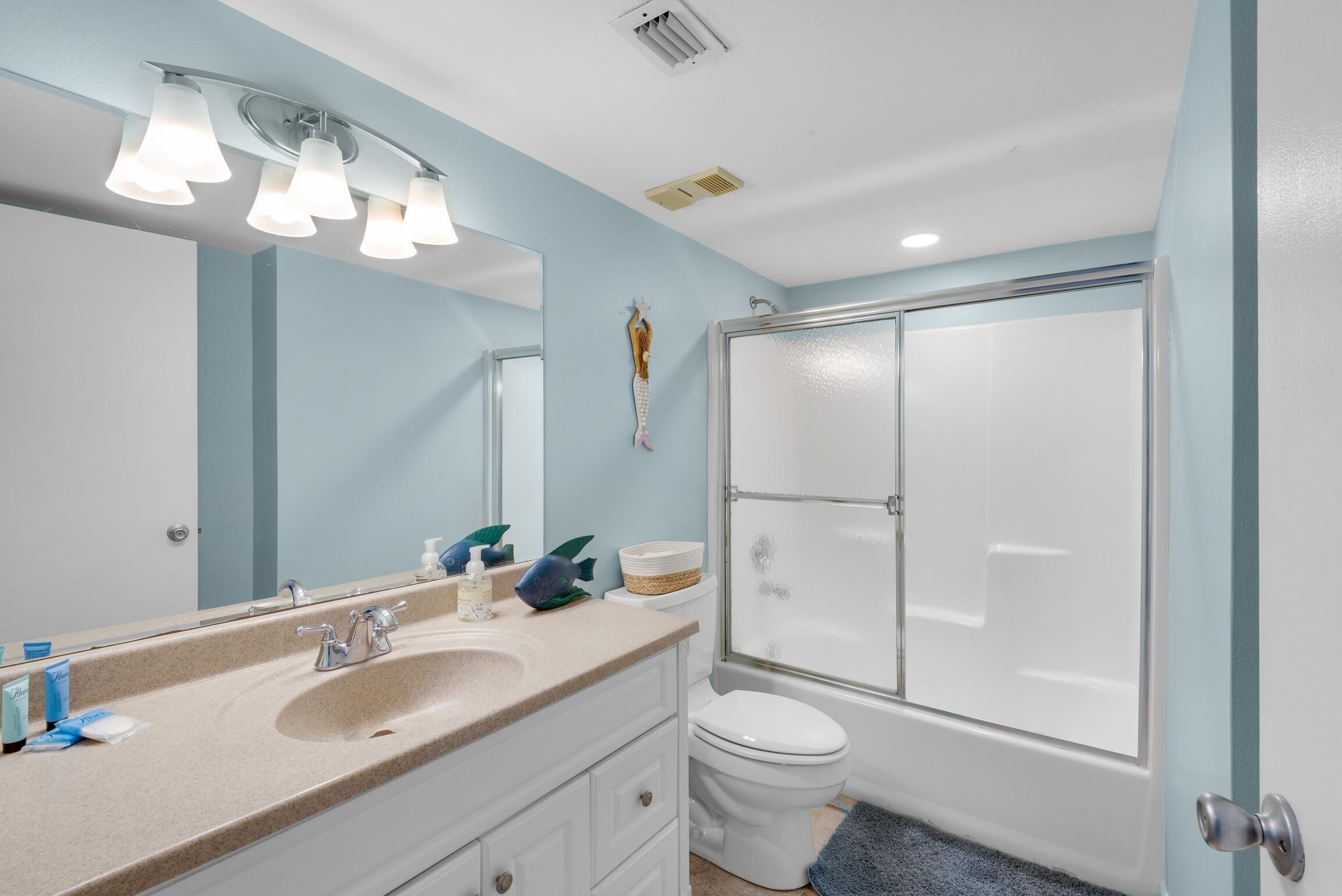 A bathroom with a sink, mirror, and toilet. There is a shower with a glass door.
