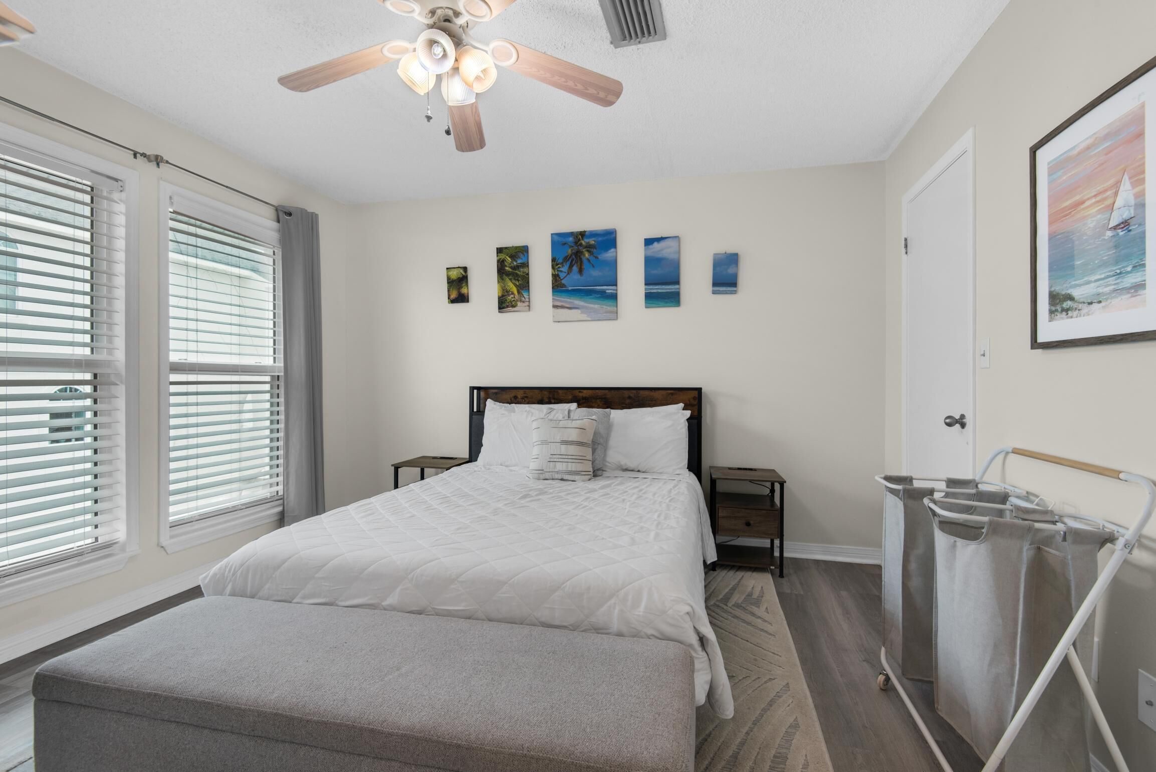 A bedroom with a bed, a ceiling fan, a nightstand, a wall-mounted trash bin, and a window with blinds.