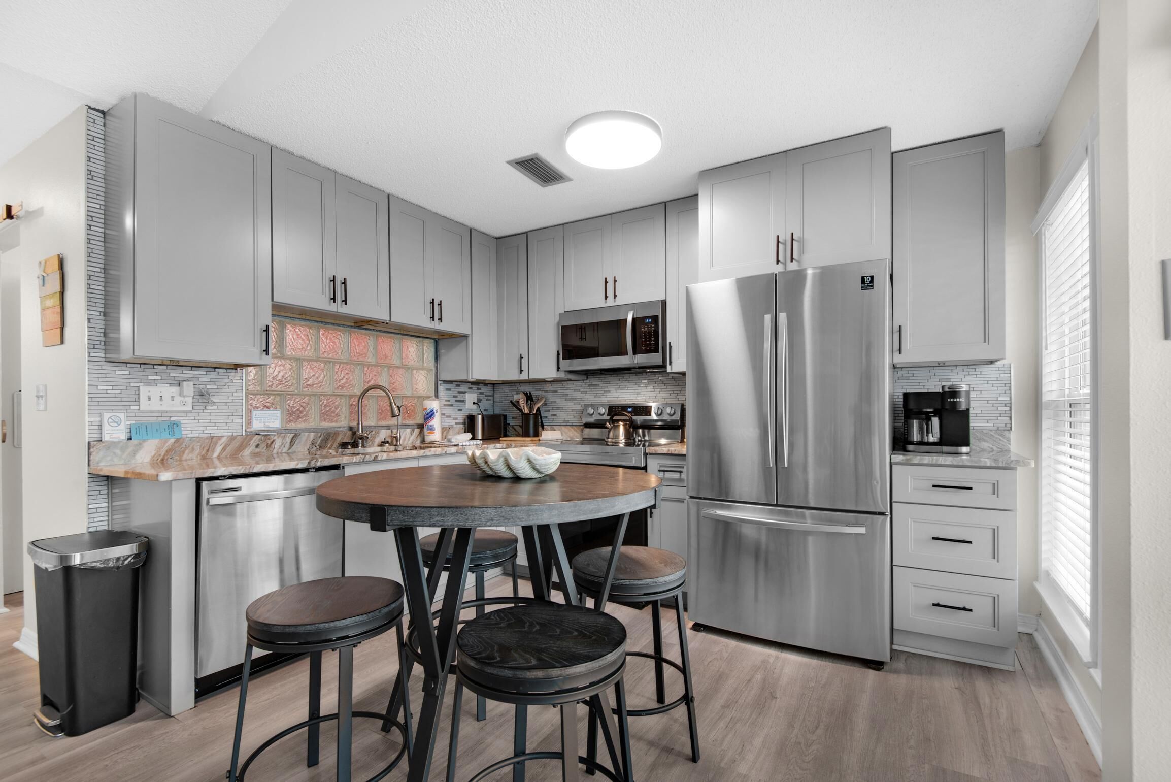 A modern kitchen with grey cabinets, stainless steel appliances, a central island with stools, and a tiled backsplash.