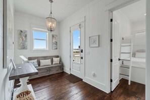 A room with a wooden floor, a bench with cushions, a chandelier, and a view through a door. - Stella Maris (Navarre)