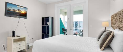 Quarto com cama, televisão, estante de livros e vista para um prédio.