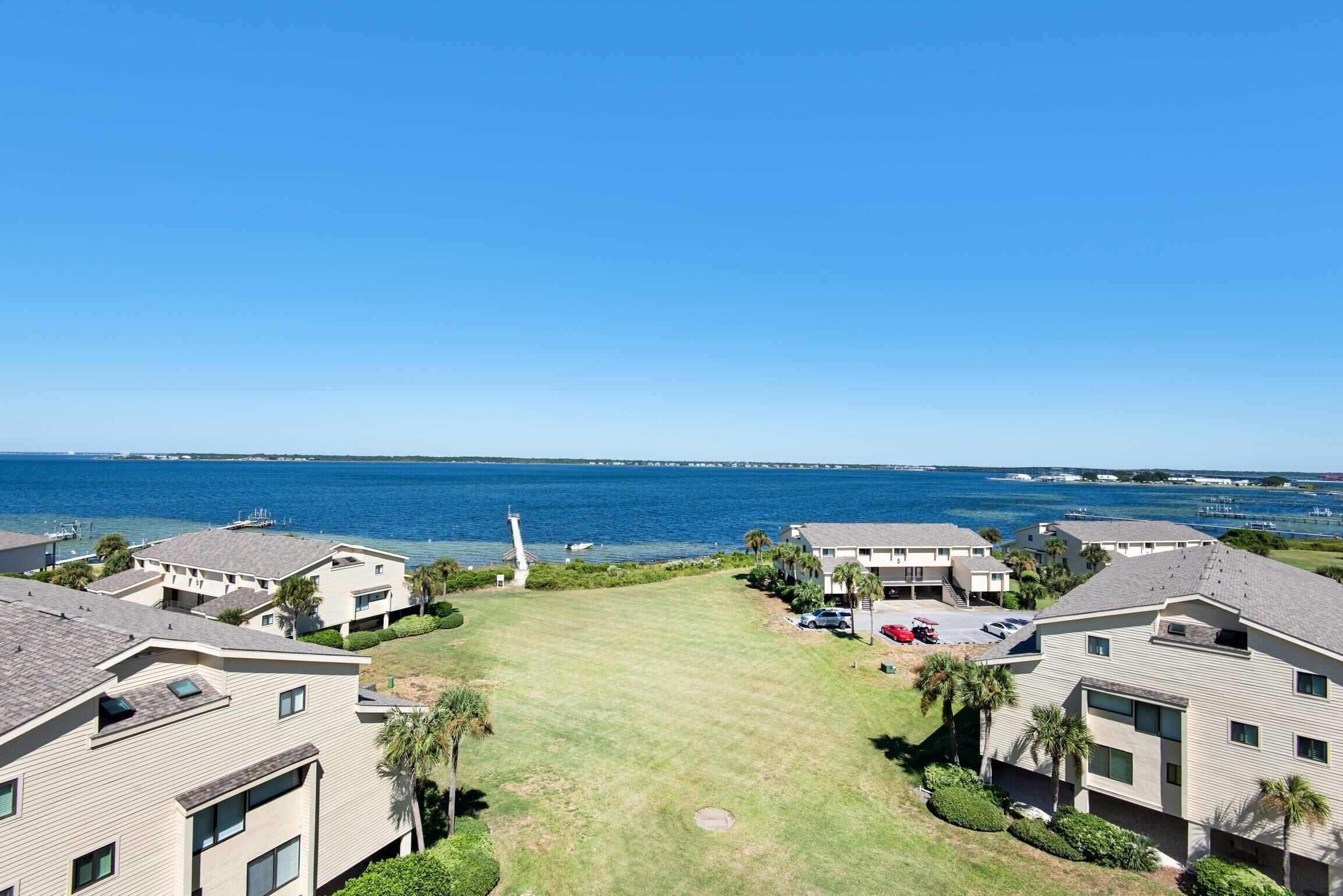 A coastal residential area with multiple two-story buildings, a grassy central area, and a view of the ocean.