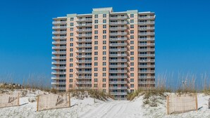 Un hôtel à plusieurs étages doté de balcons, une plage de sable en premier plan et un ciel bleu dégagé.