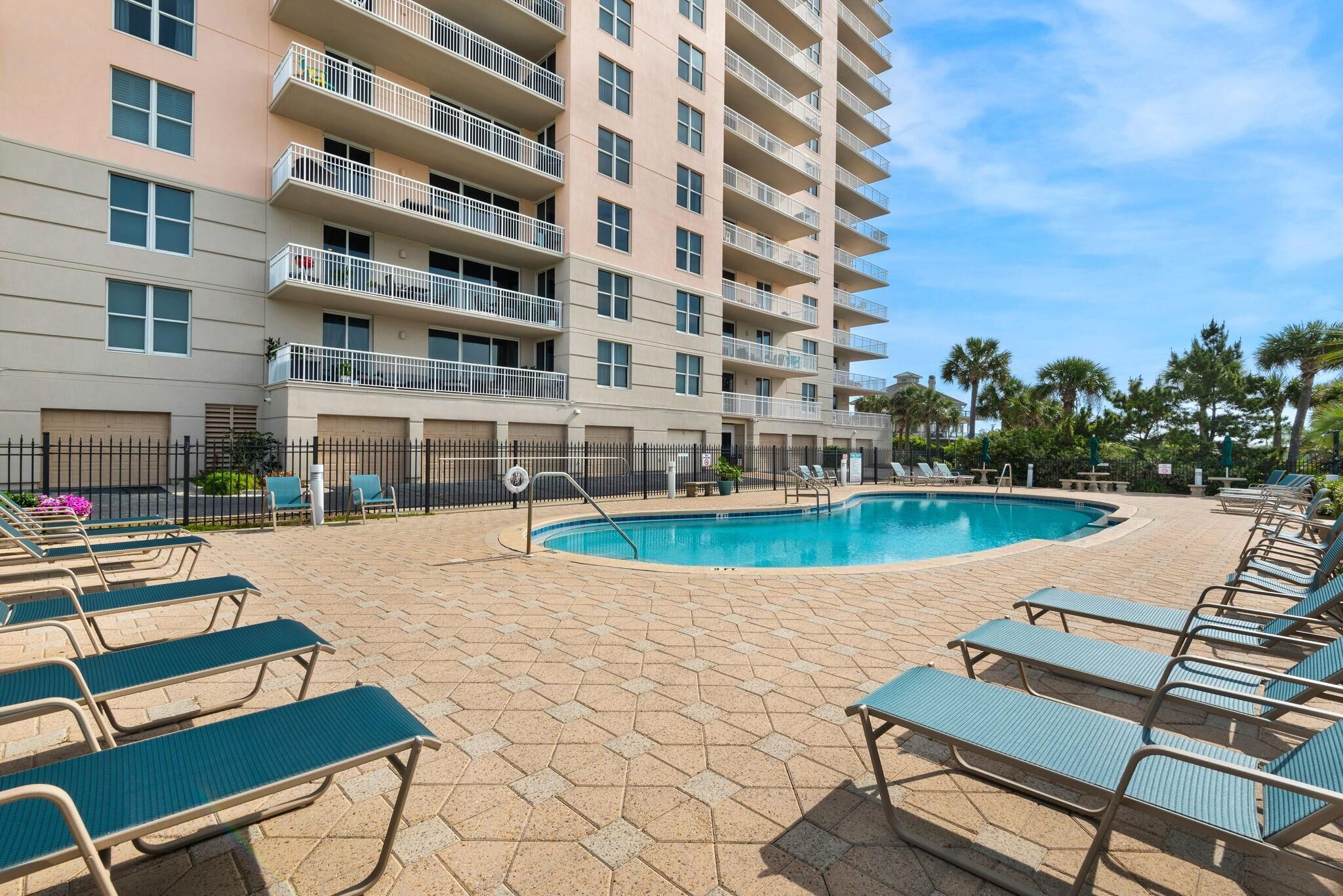 A hotel with a swimming pool, lounge chairs, and a multi-story building with balconies.