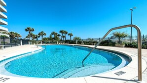 Une piscine à bord incurvé, entourée d’une clôture et de palmiers.