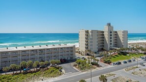A coastal hotel with multiple floors, a parking area, and a view of the ocean. - Seahorse Unit H (Pensacola Beach)