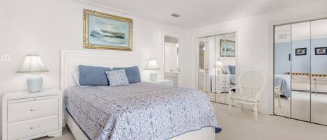 A bedroom with a large bed, white nightstands, a chair, and a wardrobe.