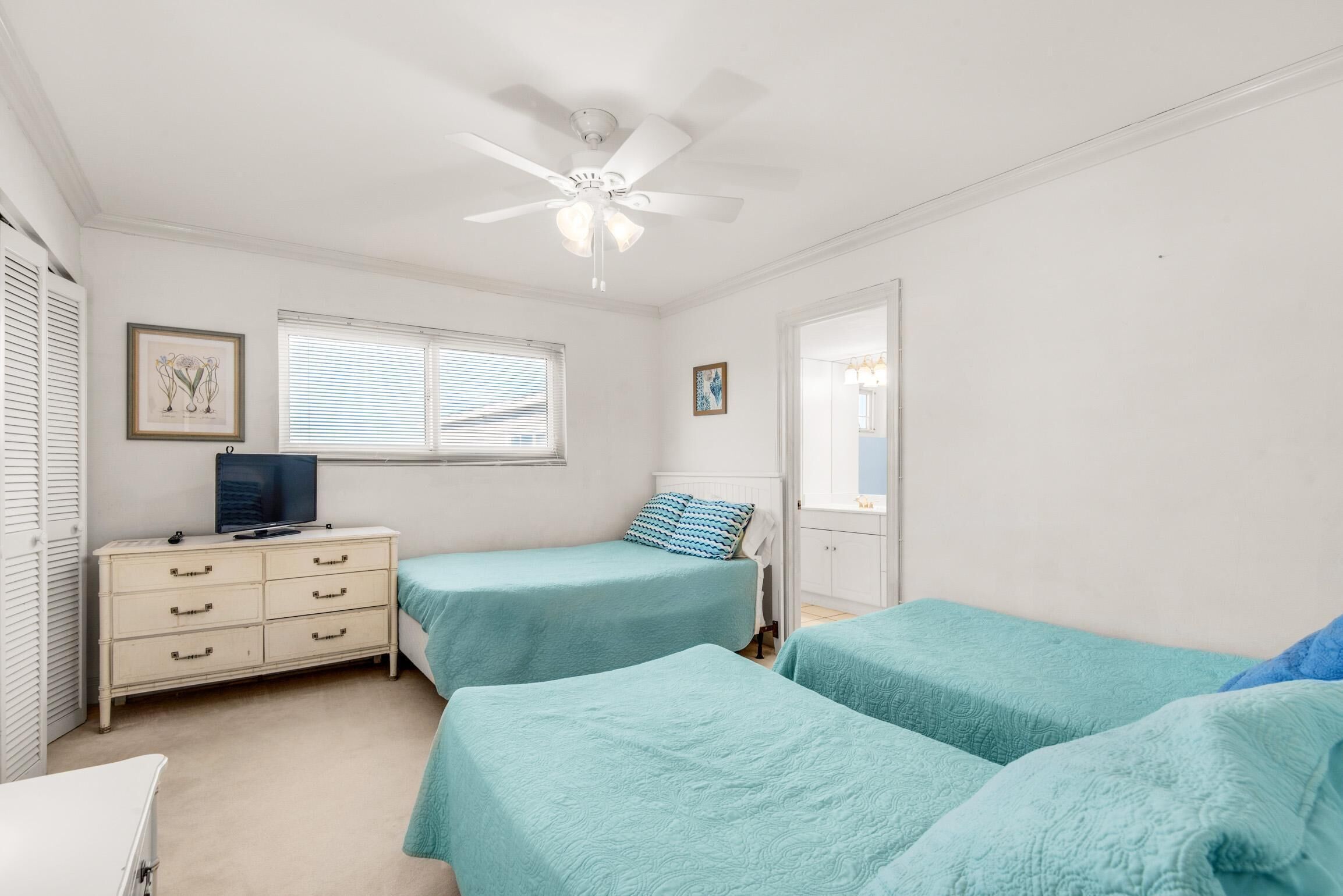 A bedroom with two beds, a dresser, a ceiling fan, and a window with blinds.