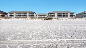 Un hôtel situé en bord de mer, avec plusieurs étages, des balcons et une promenade en bois menant à la plage.