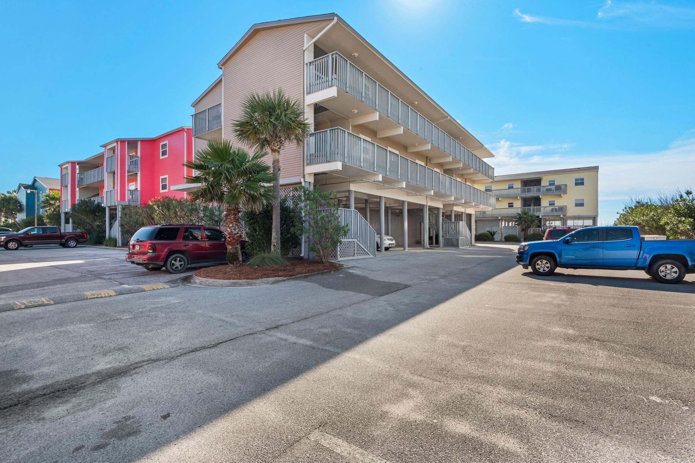 A multi-story residential building with balconies, parked cars, and a clear sky.