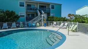 A swimming pool with lounge chairs and a staircase leading to a building with balconies.