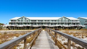 A beachfront hotel with a wooden boardwalk leading to the entrance. - White Sands 447 (Pensacola Beach)