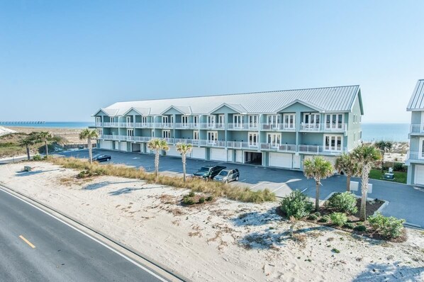 Ein Hotel direkt am Strand mit mehreren Balkonen, einem Parkplatz und einer Sandbucht.