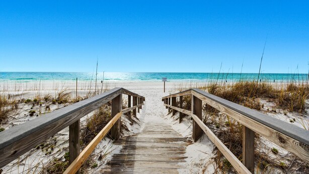 A wooden boardwalk leading to a beach with clear blue water and a clear sky. - White Sands 447 (Pensacola Beach)