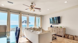 A modern living room with a sofa, a glass table, a wooden cabinet, and a TV on the wall. - White Sands 447 (Pensacola Beach)