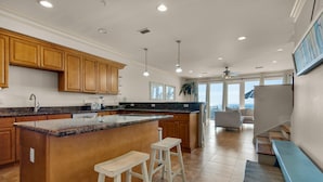 A modern kitchen with wooden cabinets, a granite countertop, and a large island with bar stools. - White Sands 447 (Pensacola Beach)