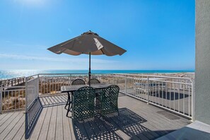 Eine Holterrasse mit Tisch, Stühlen und einem Sonnenschirm, mit Blick auf den Strand.
