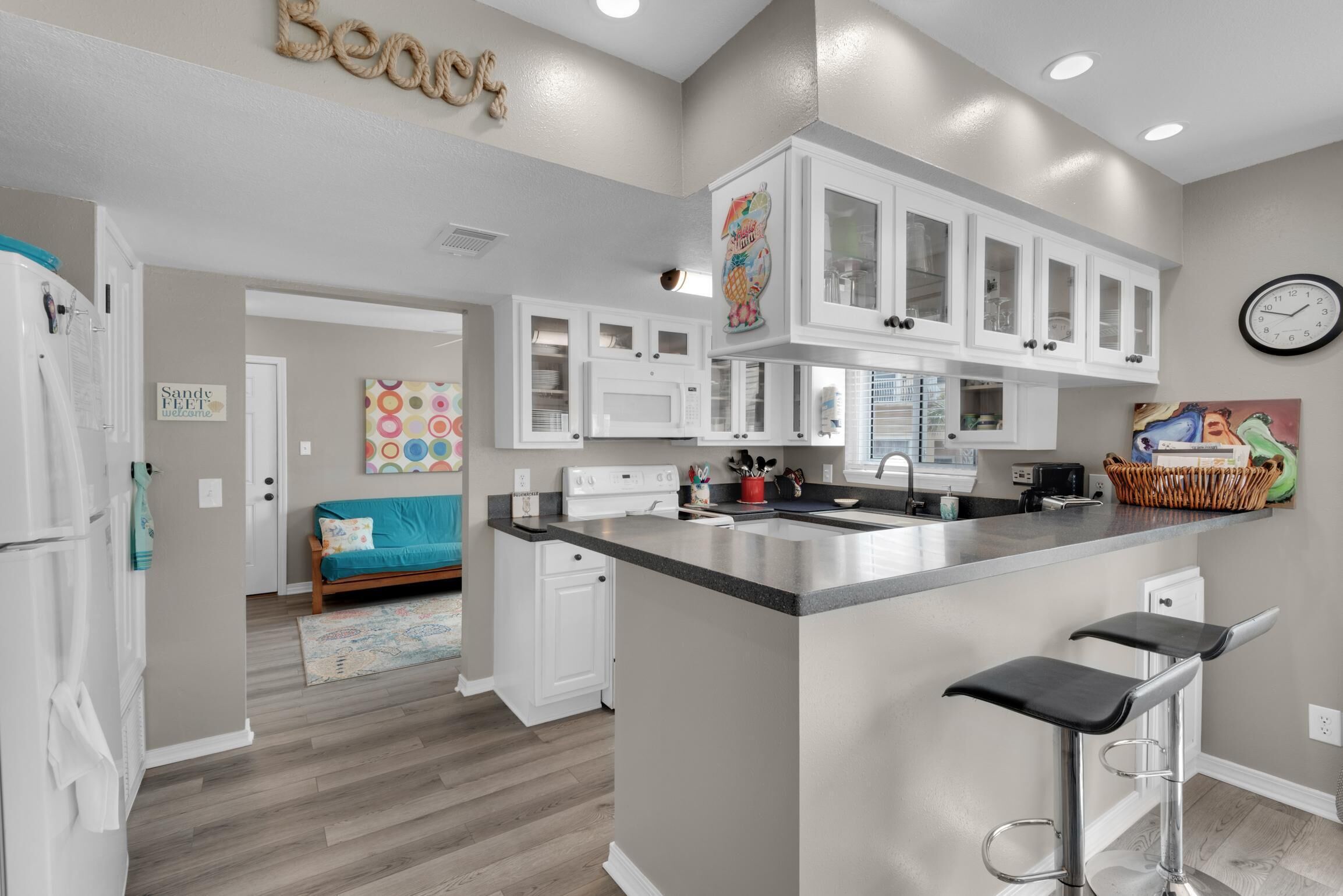A modern kitchen with white cabinets, a central island with bar stools, a microwave, and a clock on the wall.