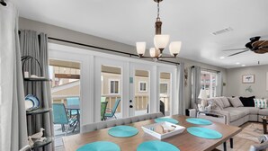 A modern living room with a wooden dining table, teal placemats, and a sofa. - Regency Cabanas E1 (Pensacola Beach)