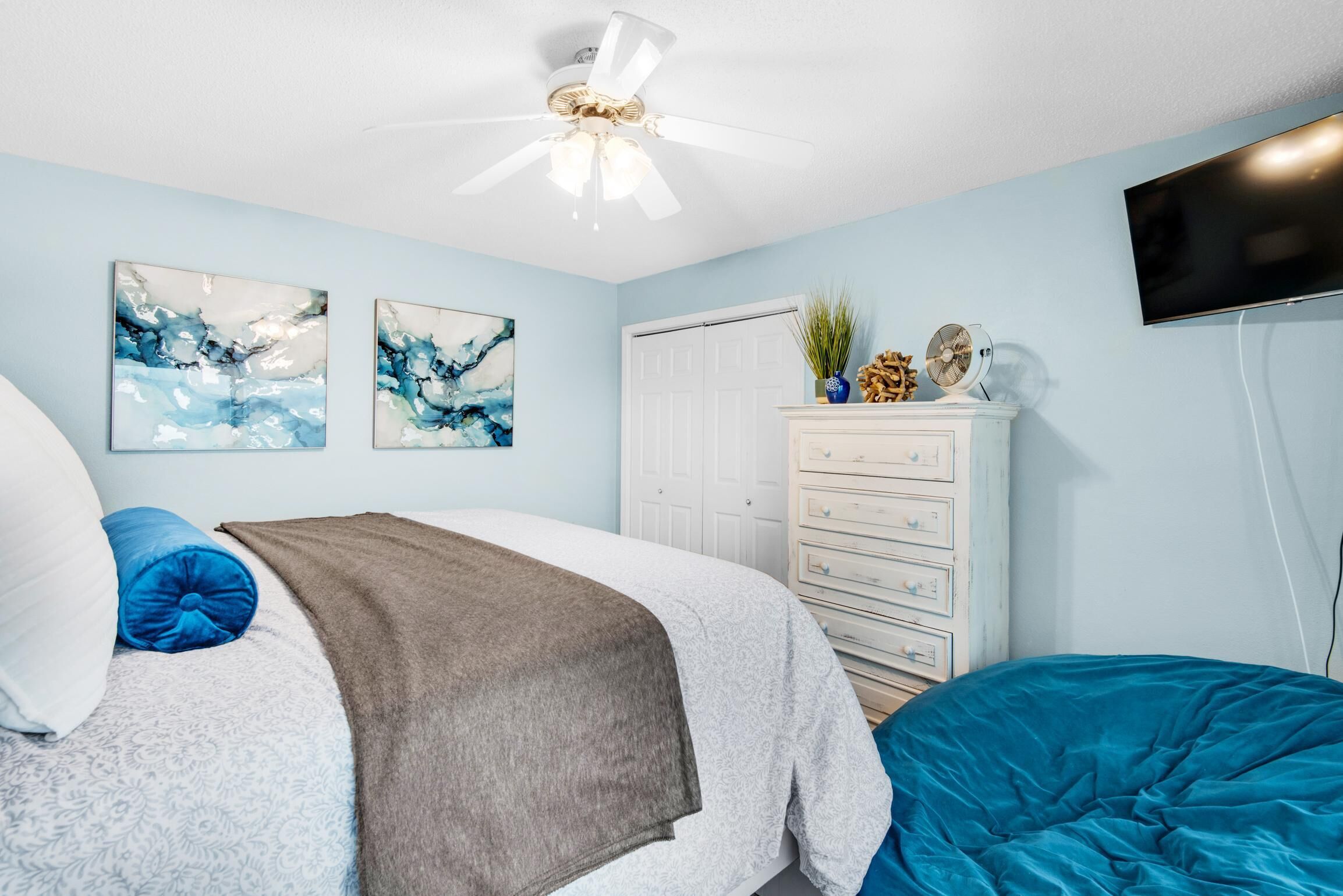 A bedroom with a bed, a dresser, a ceiling fan, and abstract wall art.