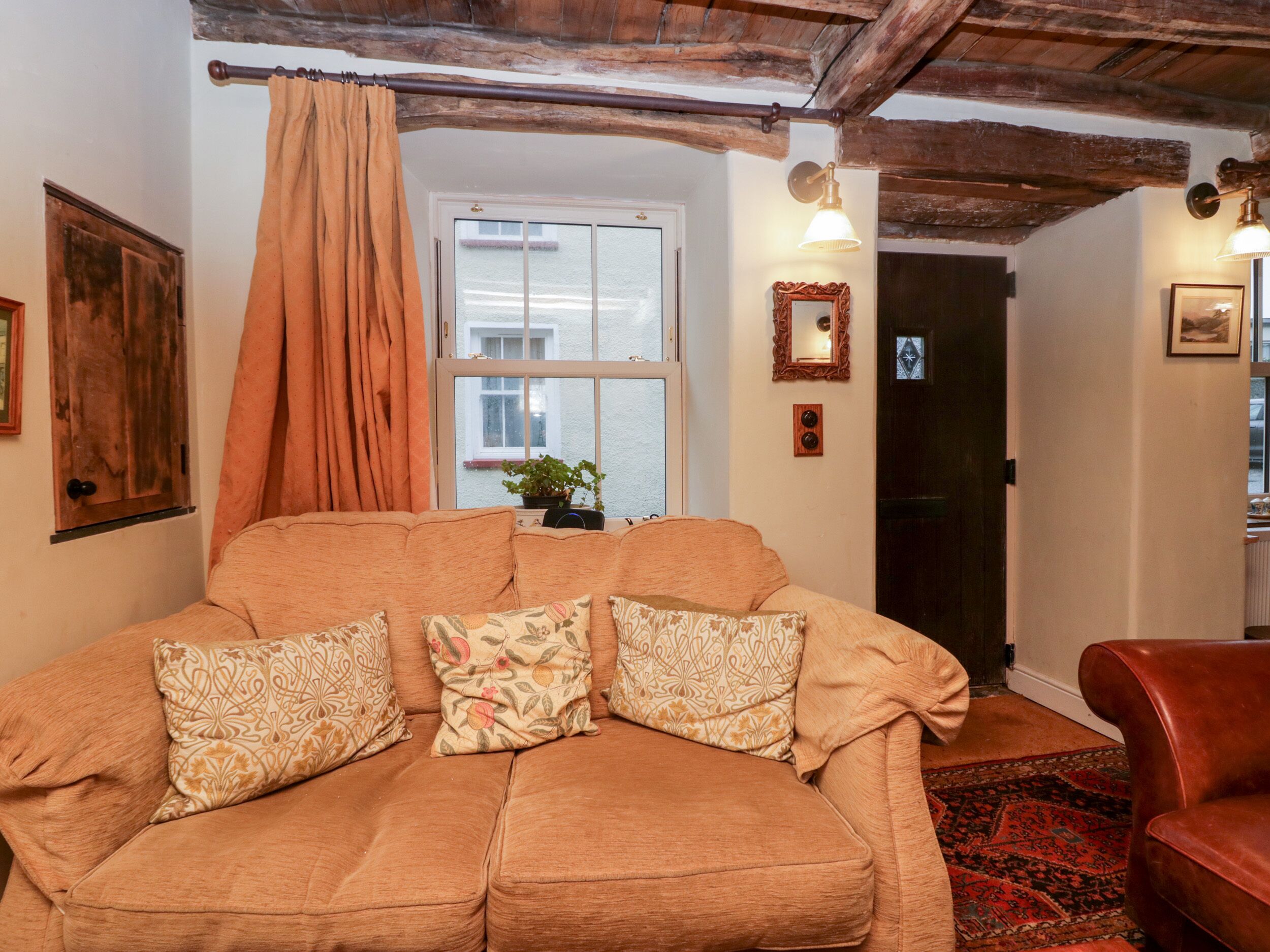 A cozy living room with a large sofa, a patterned throw pillow, a potted plant, and a wooden ceiling.