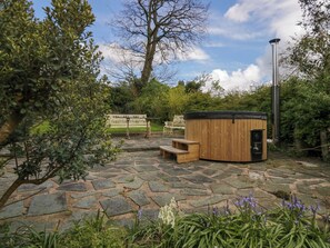 Un bain à remous dans un jardin, avec un sol en pierre, entouré de verdure et agrémenté d’un banc.