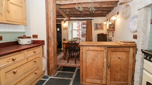A rustic kitchen with wooden cabinets, a stone floor, and a dining area with a table and chairs. - Eden Vale (Broughton in Furness)