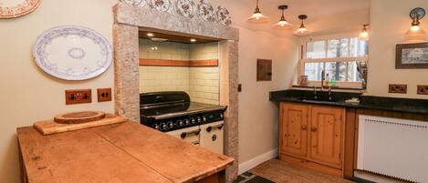 A kitchen with a stone archway, wooden cabinets, a stove, and a window.