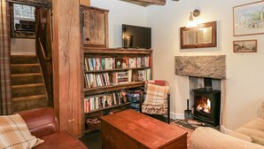 A cozy living room with a fireplace, a bookshelf, a television, and a staircase. - Eden Vale (Broughton in Furness)