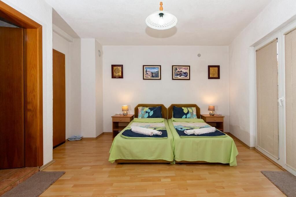 A bedroom with two beds, wooden flooring, a ceiling light, and framed pictures on the wall.