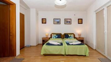A bedroom with two beds, wooden flooring, a ceiling light, and framed pictures on the wall.
