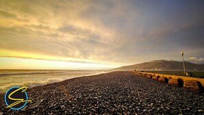 A pebbled beach with a rocky shoreline, a distant mountain, and a lighthouse. - The Springfield Fairbourne (Fairbourne)