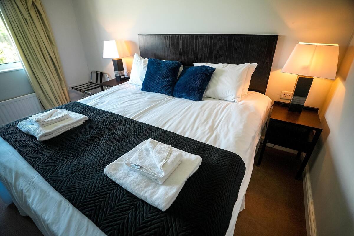 A neatly made bed with white and blue pillows, a black headboard, and two bedside lamps.
