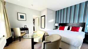 A hotel room with a large bed, a desk with a chair, a glass table, and a striped wall. - The Springfield Fairbourne (Fairbourne)