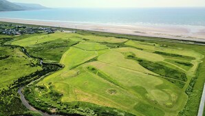 An aerial view of a golf course with a beach in the background. - The Springfield Fairbourne (Fairbourne)